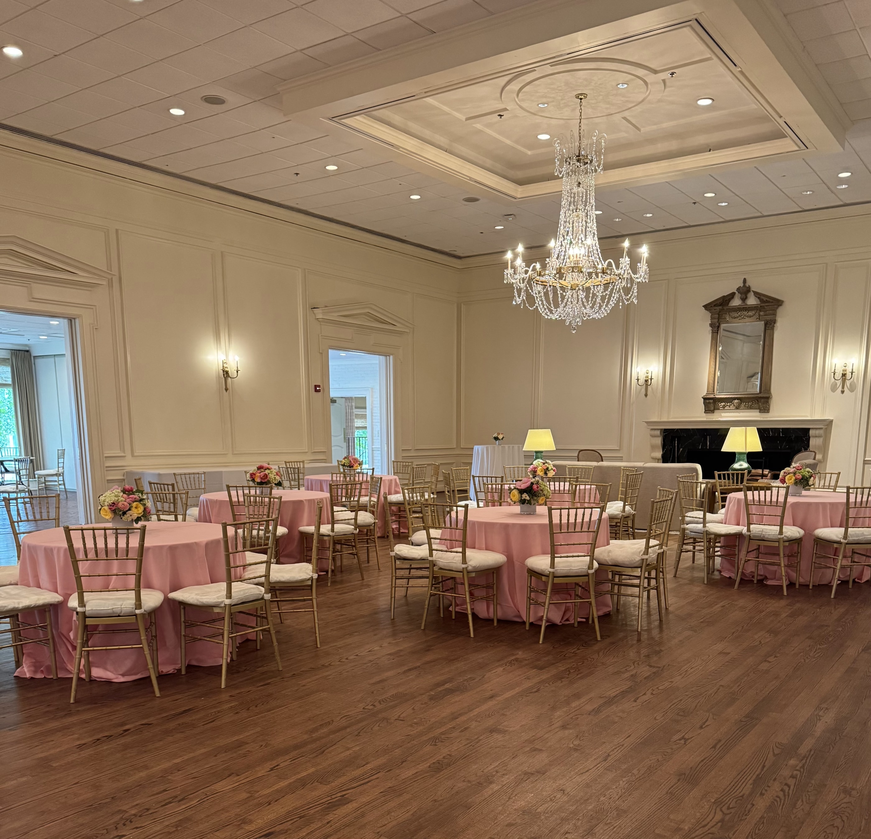 A gentle reception room with soft pink linens, gold chairs and small pastel centerpieces beneath a chandelier