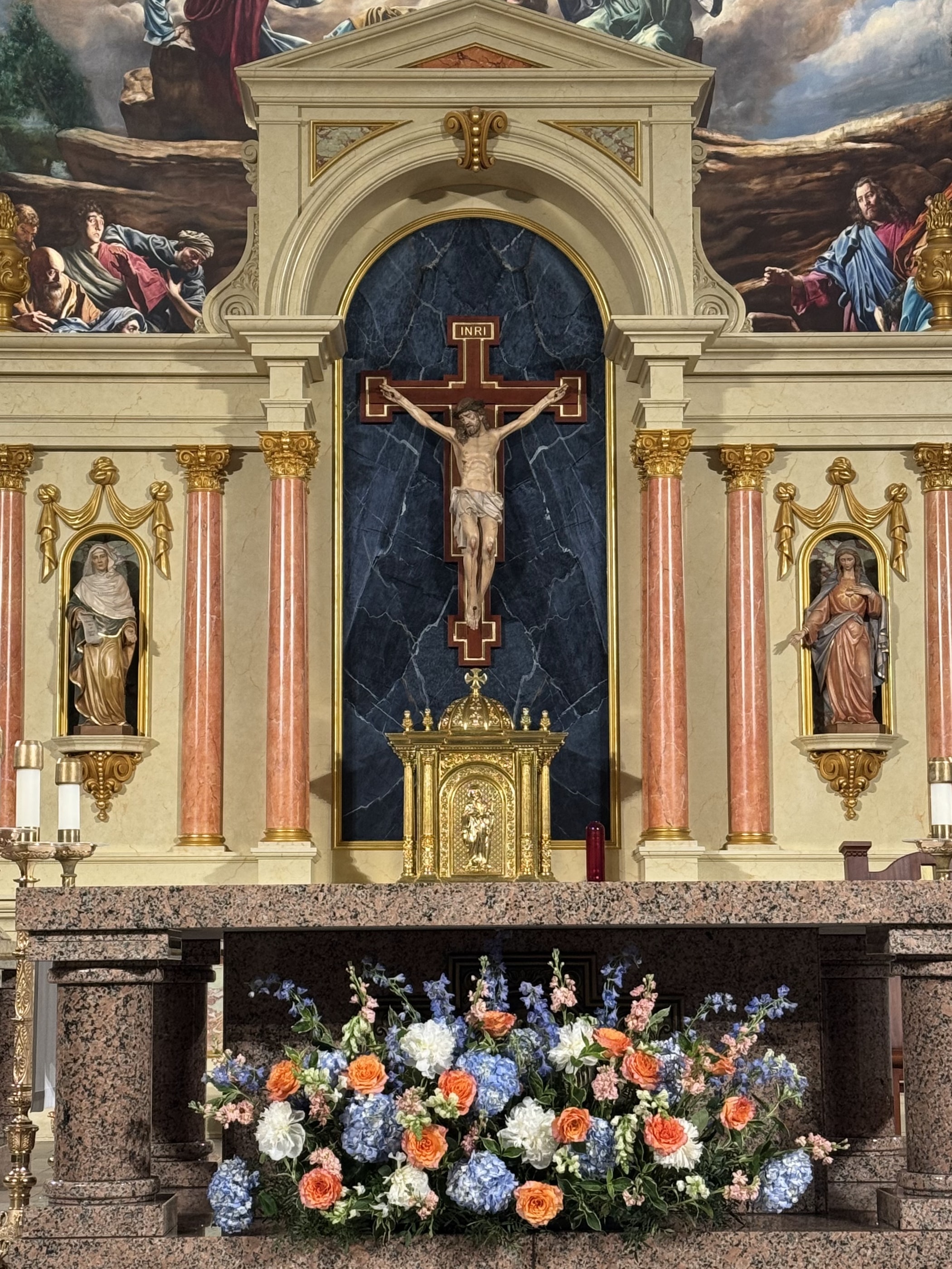 A low arrangement of blue hydrangea, white and coral roses set before an ornate church altar