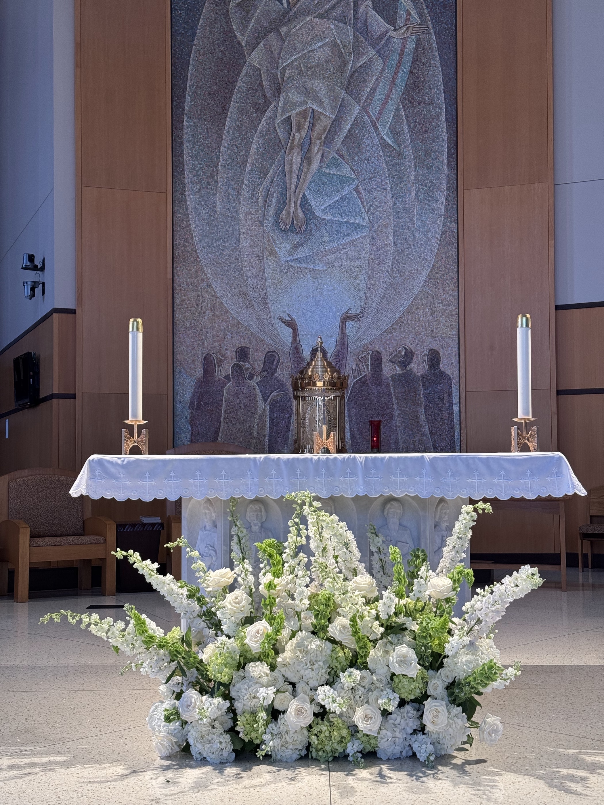 A wide all-white arrangement of roses, stock and hydrangea at the foot of a church altar