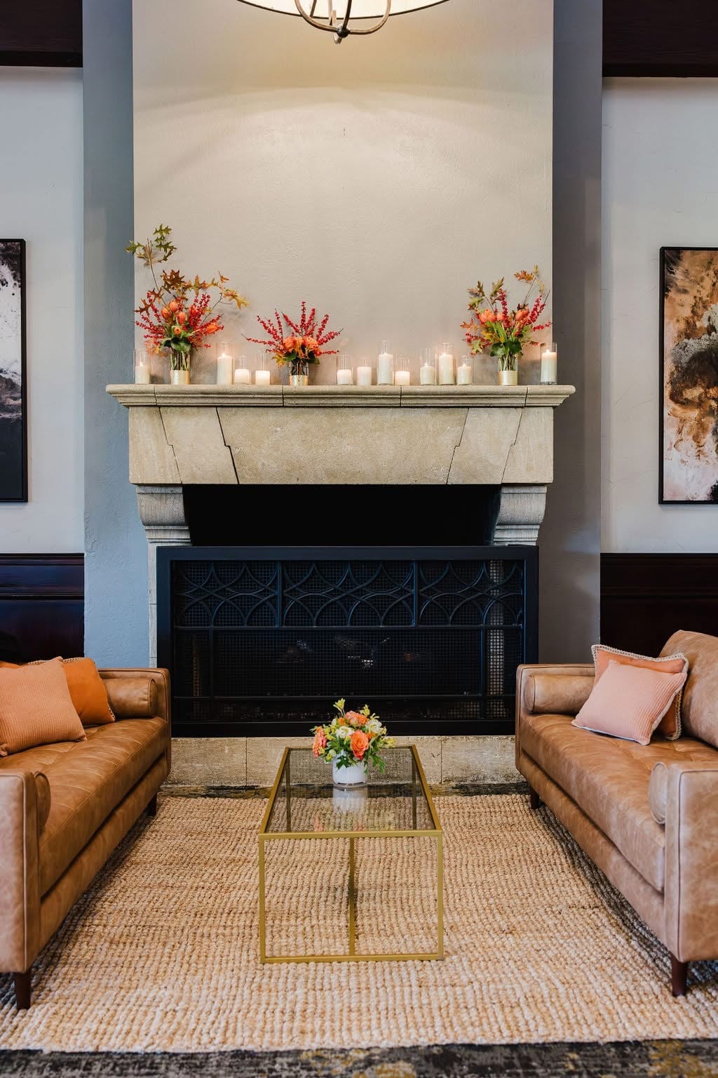 A stone fireplace mantel lined with coral and orange arrangements and pillar candles above a leather-seated lounge