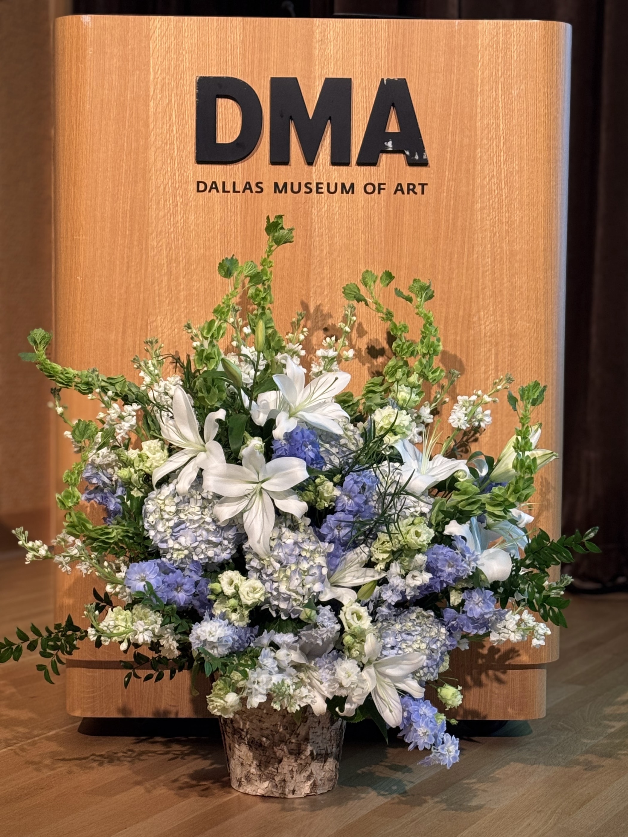 A blue and white arrangement of lilies, delphinium and stock at the base of the Dallas Museum of Art podium