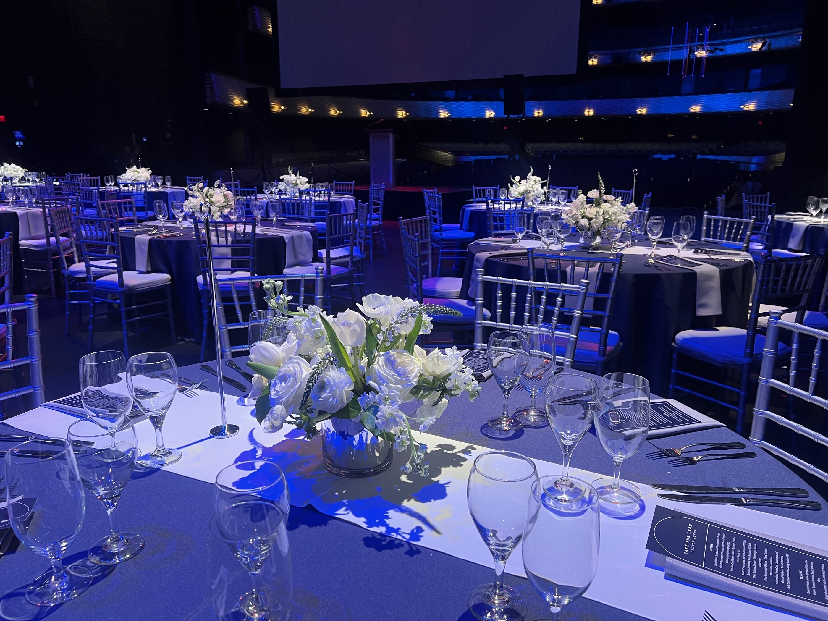 Gala tables under deep blue stage lighting at the Winspear Opera House, each with a low white and blue centerpiece