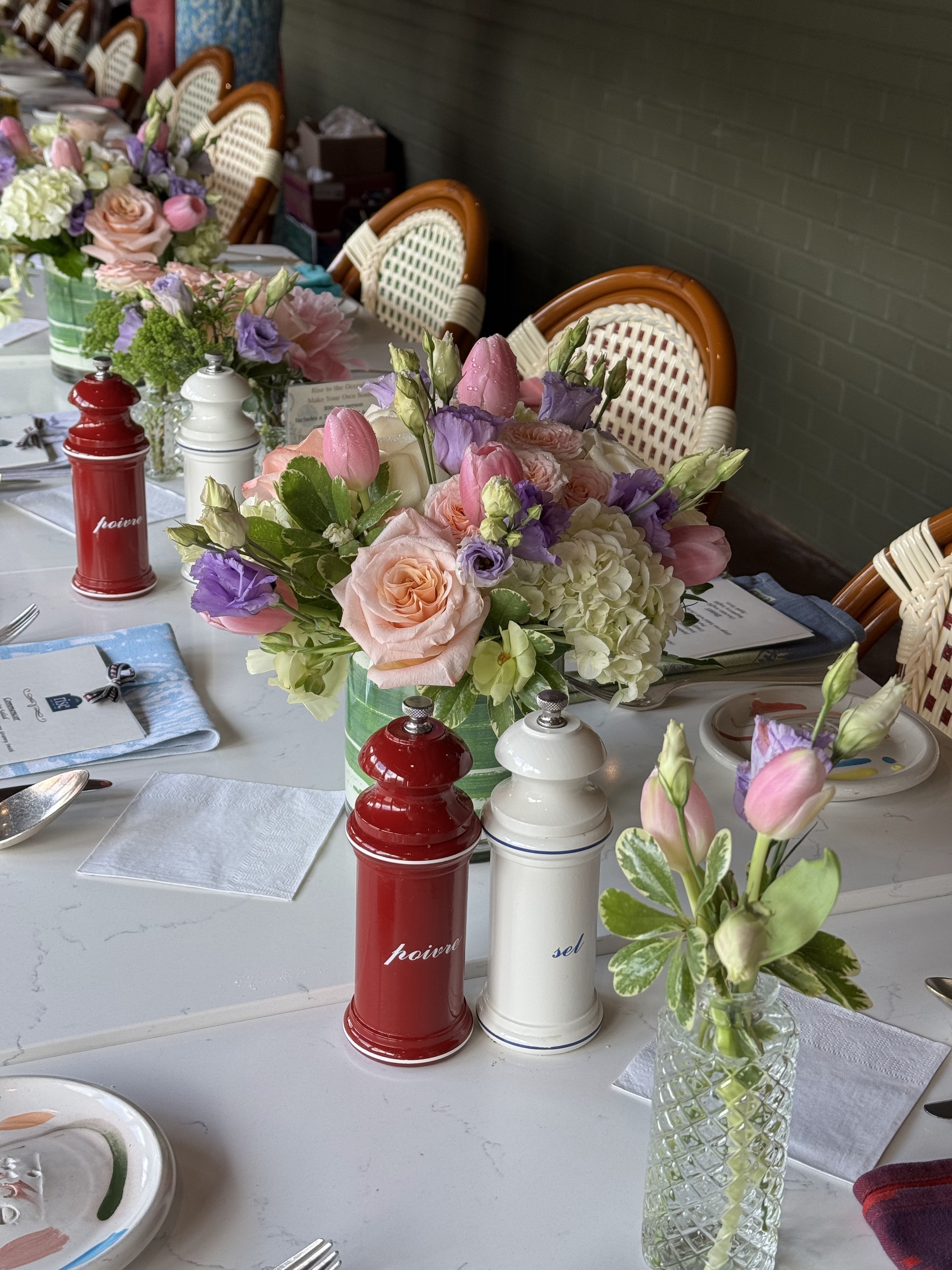 A bridal luncheon table with pastel arrangements of peach roses, purple lisianthus and pink tulips beside rattan bistro chairs
