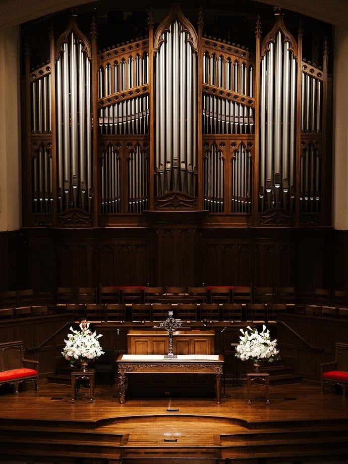 Two white lily arrangements flanking the communion table beneath the pipe organ at Park Cities Presbyterian Church