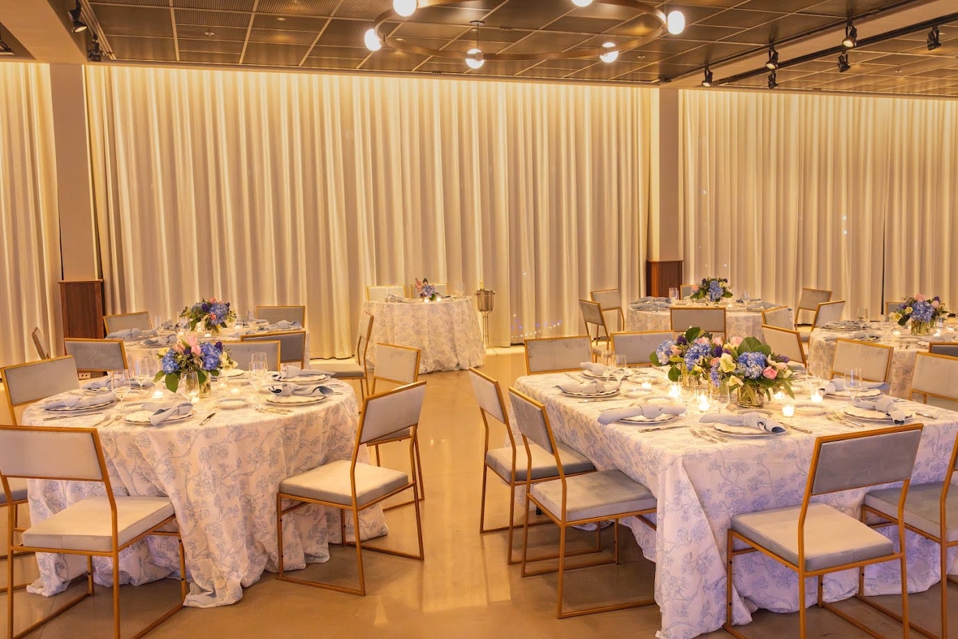 Reception room draped in ivory with blue and white low centerpieces on lace-overlaid tables and gold chairs
