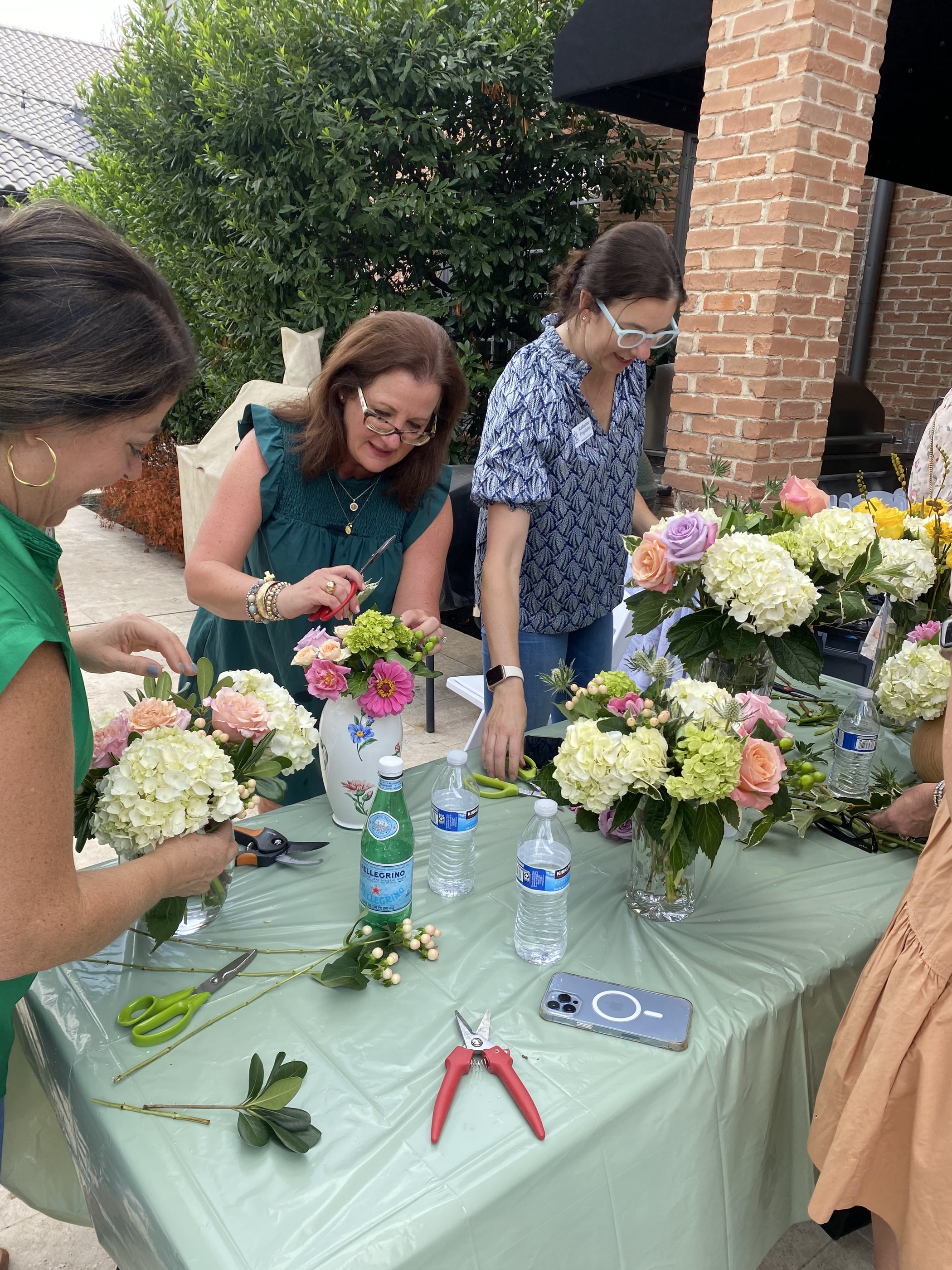 Workshop guests trimming stems and building arrangements around an outdoor table of hydrangea and roses