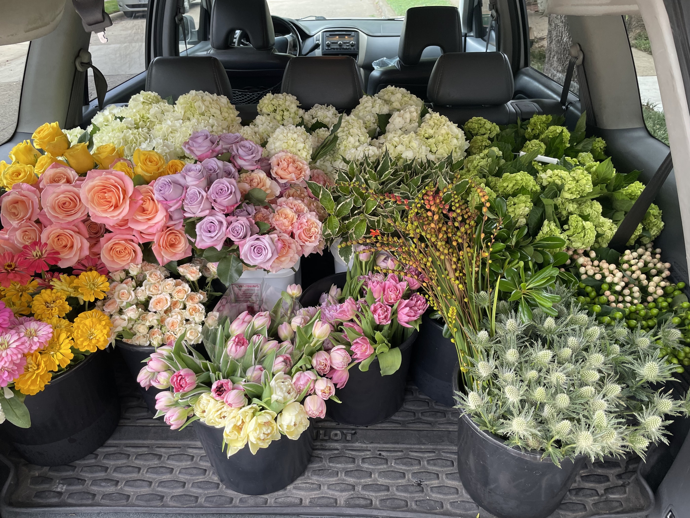 Buckets of roses, tulips, hydrangea and thistle loaded in the back of a vehicle before a floral workshop