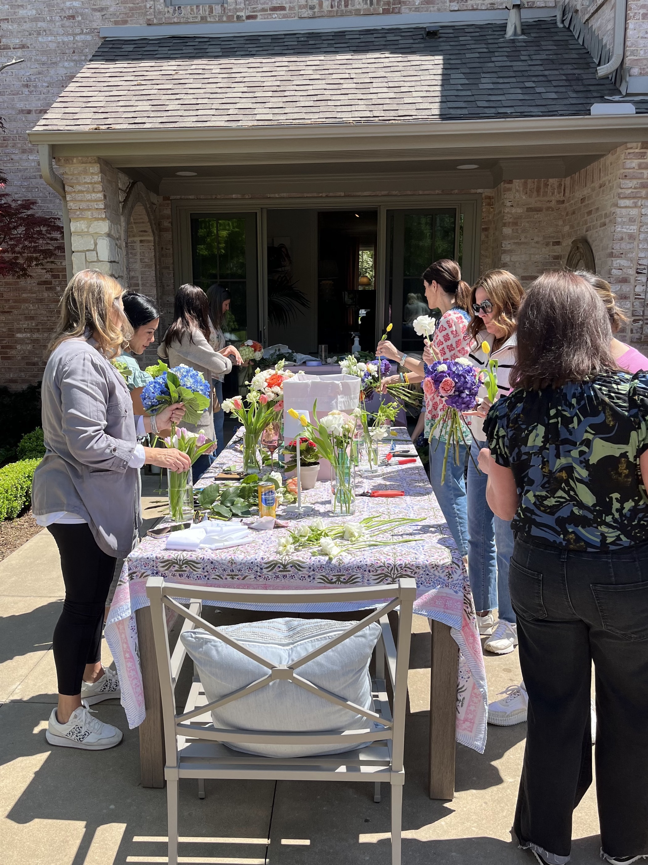 Guests gathered along a long patio table arranging flowers into vases at a floral workshop